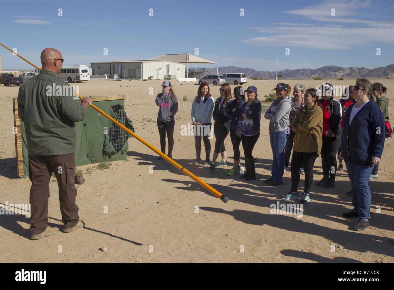 Dave Andrew, counter Improvised Explosive Device instructor, Marine Corps Engineer School, teaches ITX for Spouses participants how to use a Holley stick at Range 800 aboard Marine Corps Air Ground Combat Center, Twentynine Palms, Calif., March 30, 2017. The Holley stick is a tool used exclusively by Marine Corps explosive ordnance disposal technicians that provides them with the capability to investigate and manipulate a suspect IED from a stand-off distance. Stock Photo