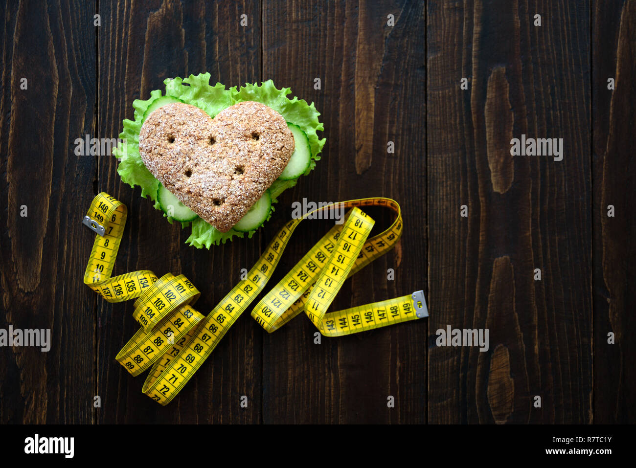 Healthy heart shape sandwich with salad and cucumbers. Dieting concept. Wooden background. Measuring tape Stock Photo