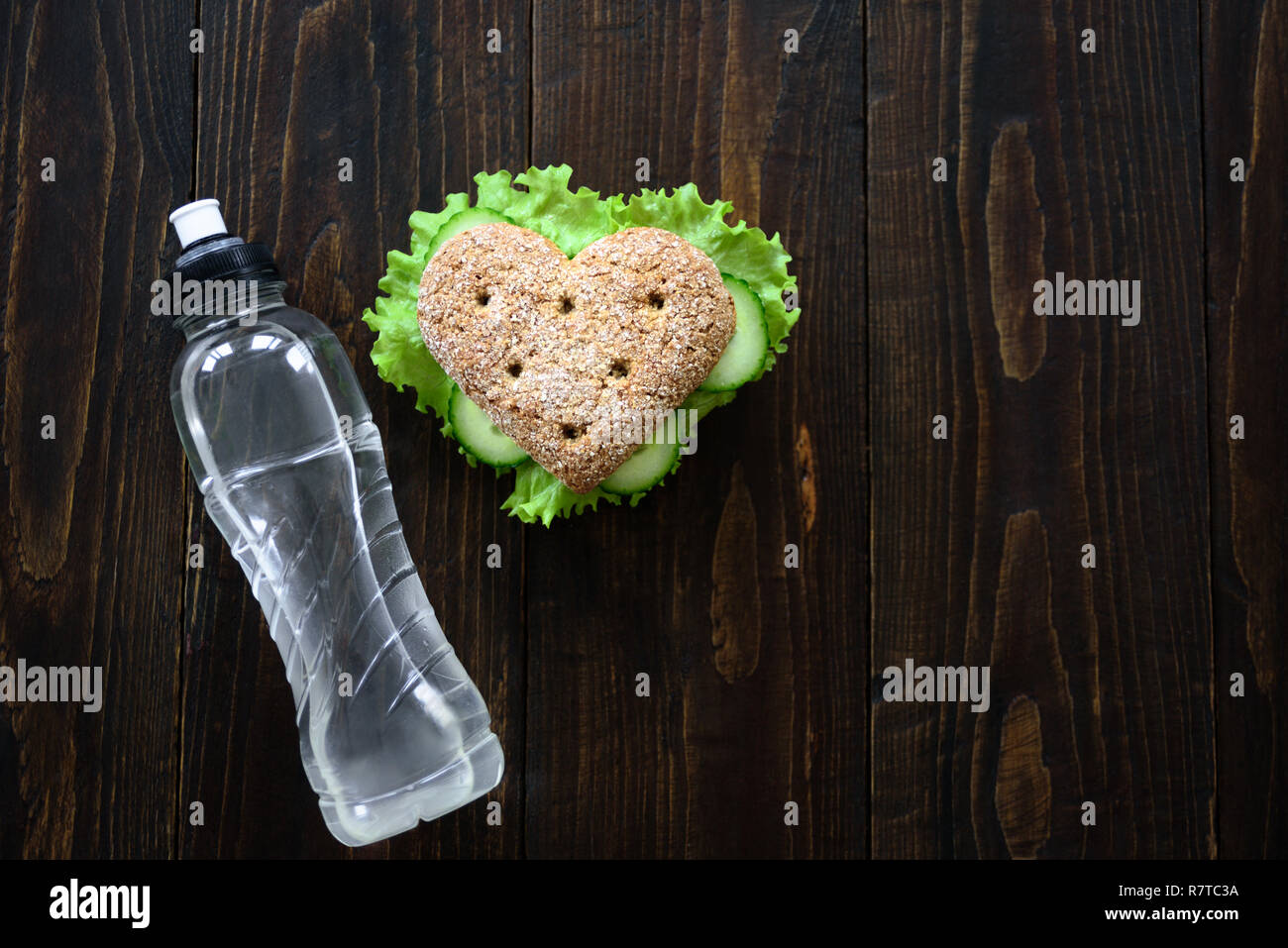 Healthy heart shape sandwich with salad and cucumbers. Dieting concept. Wooden background. Water bottle Stock Photo