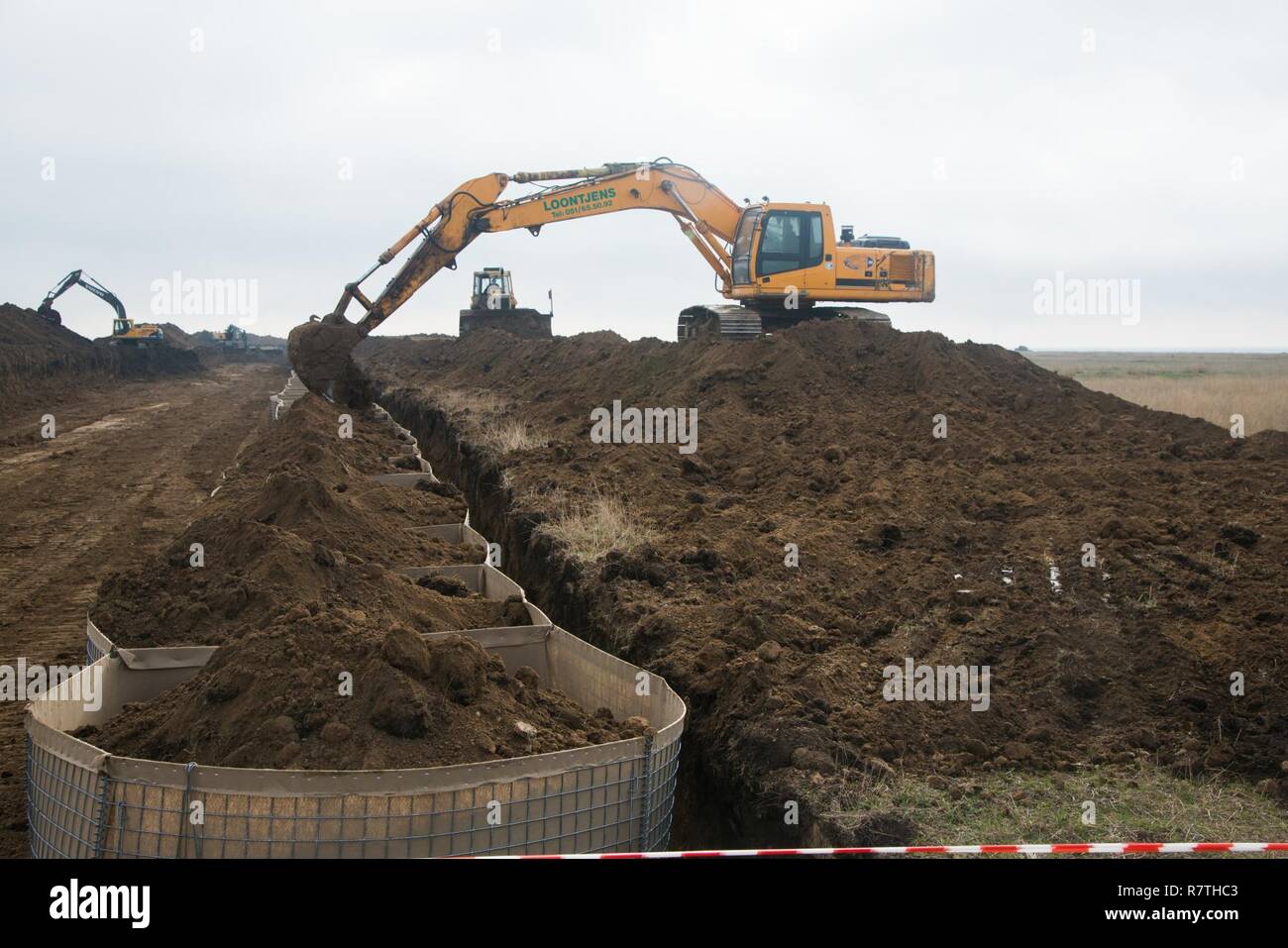 A contractor using an excavator fills the HESCO defensive barriers to be  used as a protective barrier with dirt for the installation of the Theissen  Mover Armor Target (MAT) system, April 6,