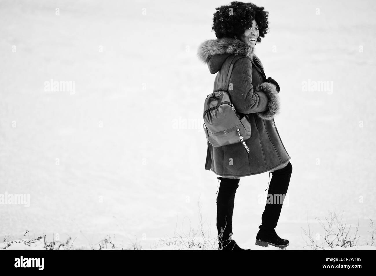 Curly hair african american woman wear on sheepskin coat and gloves with backpack posed at winter day. Stock Photo