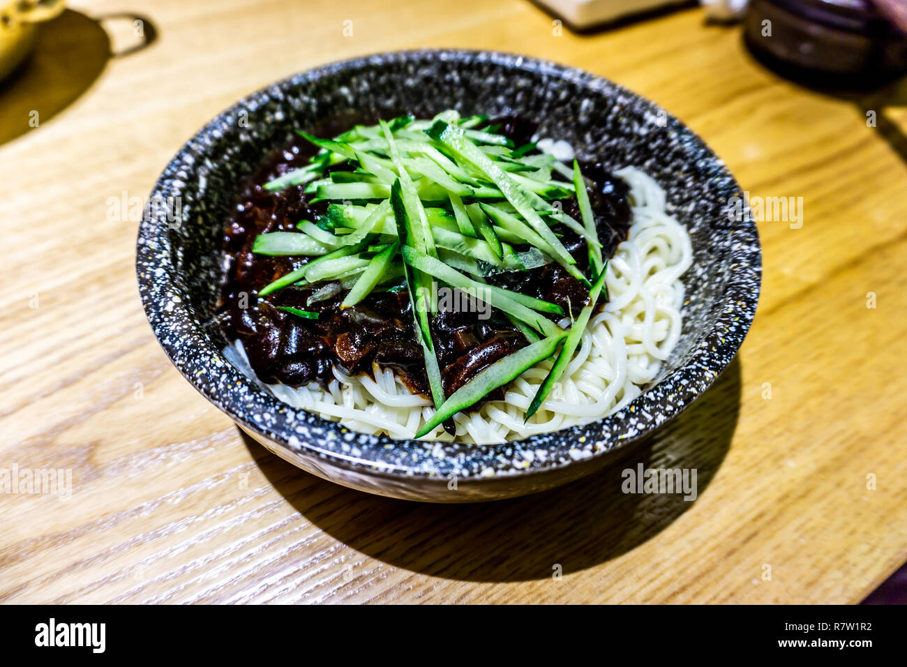 Korean Jajangmyeon Dish Served in a Stone Bowl Garnished with Cucumber Stock Photo
