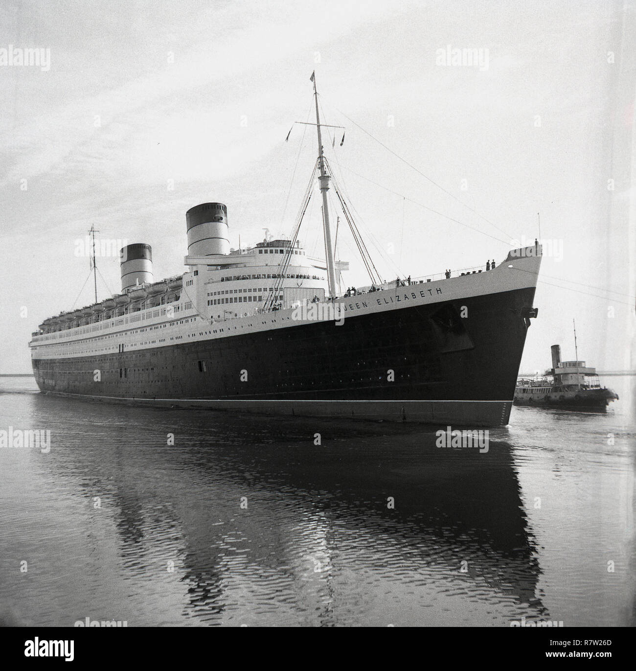 1950s, historical, The RMS Queen Elizabeth being brought into dock by a tugboat. The steamship was an ocean liner that provided a luxury liner service bewtween Southampton and New York City in the USA, via Cherbourg in France. Built by John Brown & Co at Clydebank, Scotland, when launched in 1938, she was the largest passenger liner ever built and remained so for 56 years thereafter. She was used as a troopship in WW2. Stock Photo