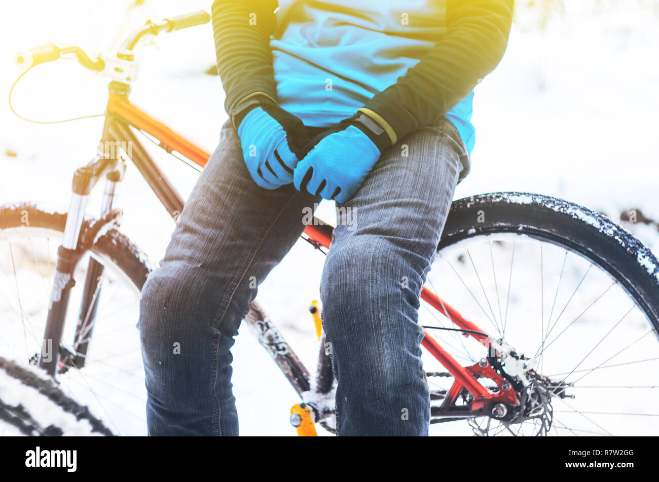 Rider in a blue jersey and blue gloves sitting on the bicycle frame in snowy forest. Rest during training concept. Detailed of extreme sport backgroun Stock Photo