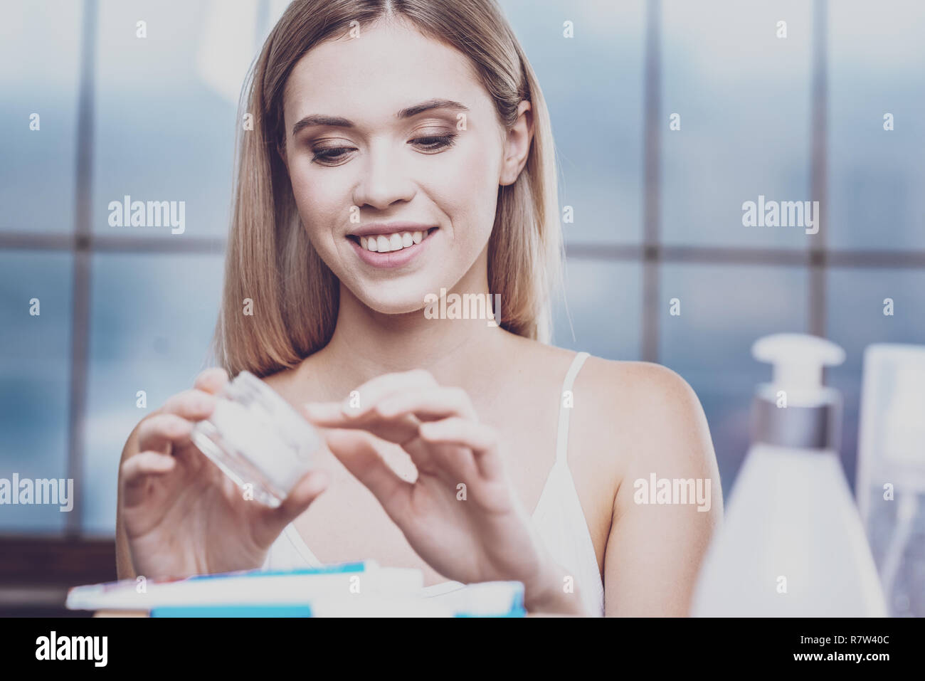 Pleasant young woman looking into a jar of face cream Stock Photo