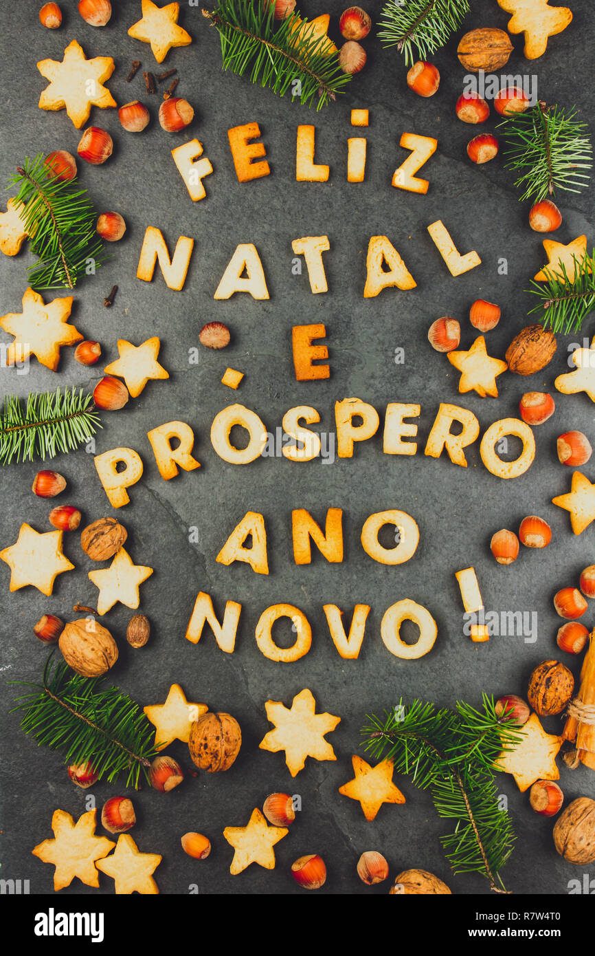 FELIZ NATAL COOKIES. Words Merry Christmas and Happy New Year en portuguese  with baked cookies, Christmas decoration and nuts on black slate  background. Christmas card for portuguese speaking countries top view Stock