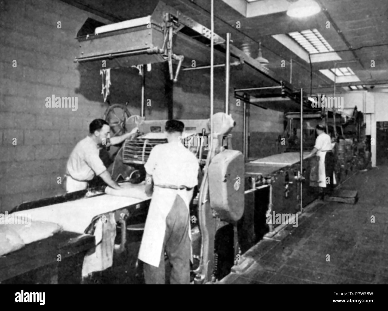 An old photograph showing biscuit dough being processed by passing it by hand through a Break Machine at Huntley and Palmer's UK biscuit factory at Reading,Berkshire. (Once the world’s largest biscuit factory) Stock Photo