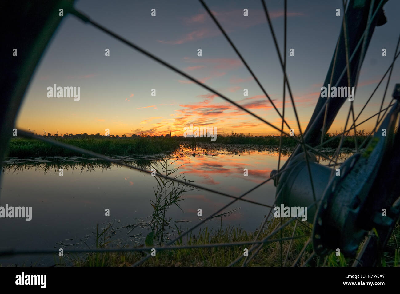 A beautiful sunset with reflections in the water of a lake, as seen through the wheel of a bicycle Stock Photo