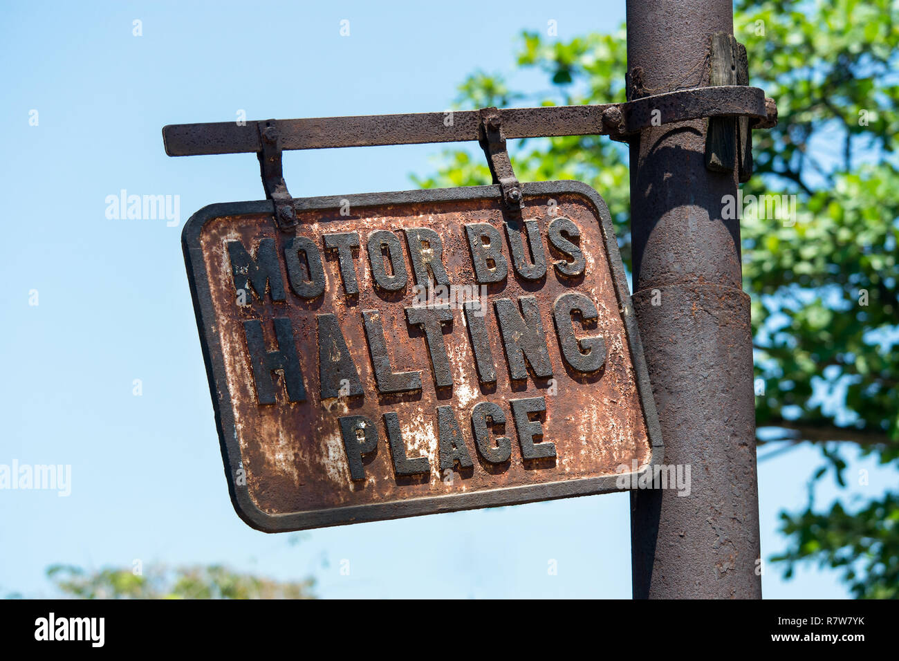 An old disused rusting metal Bus Stop sign hangs wonky from a weather post, reading ' Motor Bus Halting Place., Stock Photo