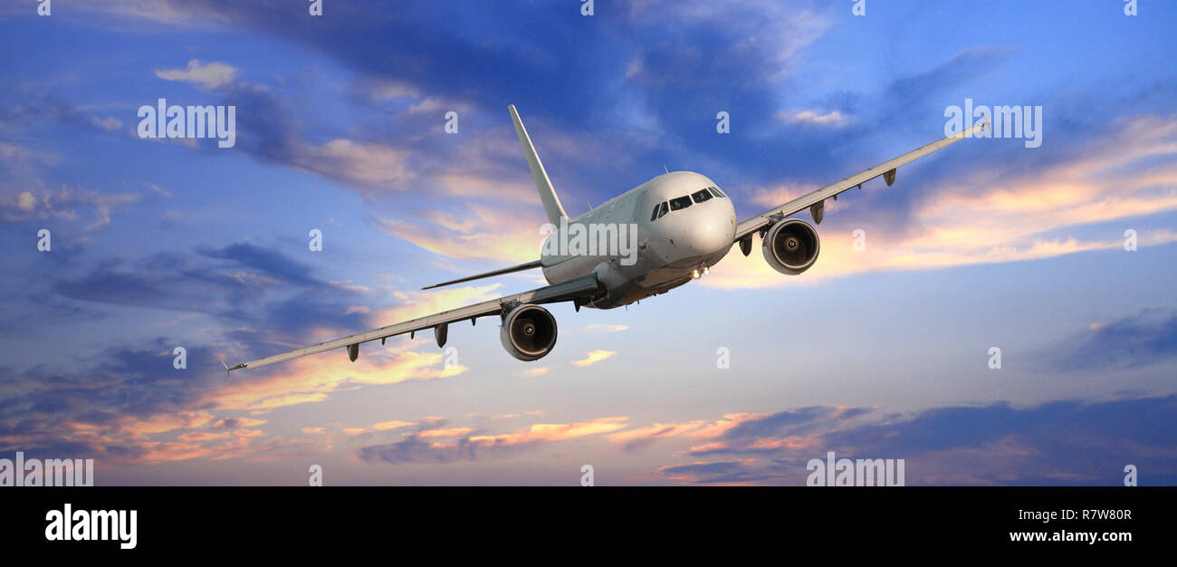 Commercial airplane flying above clouds in dramatic sunset light Stock Photo