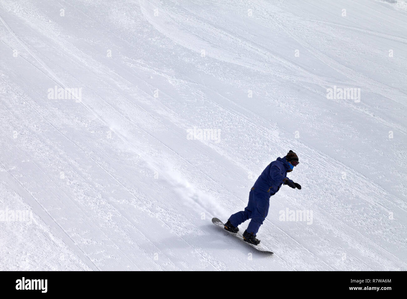 Snowboarder downhill on snow grooming ski slope at cold winter day ...