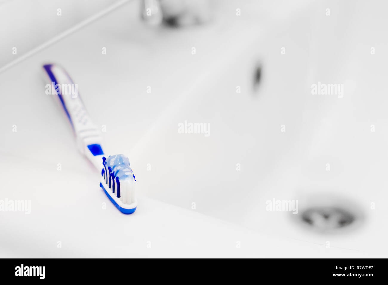 Toothbrush with toothpaste on washbasin. Small depth of field. Stock Photo