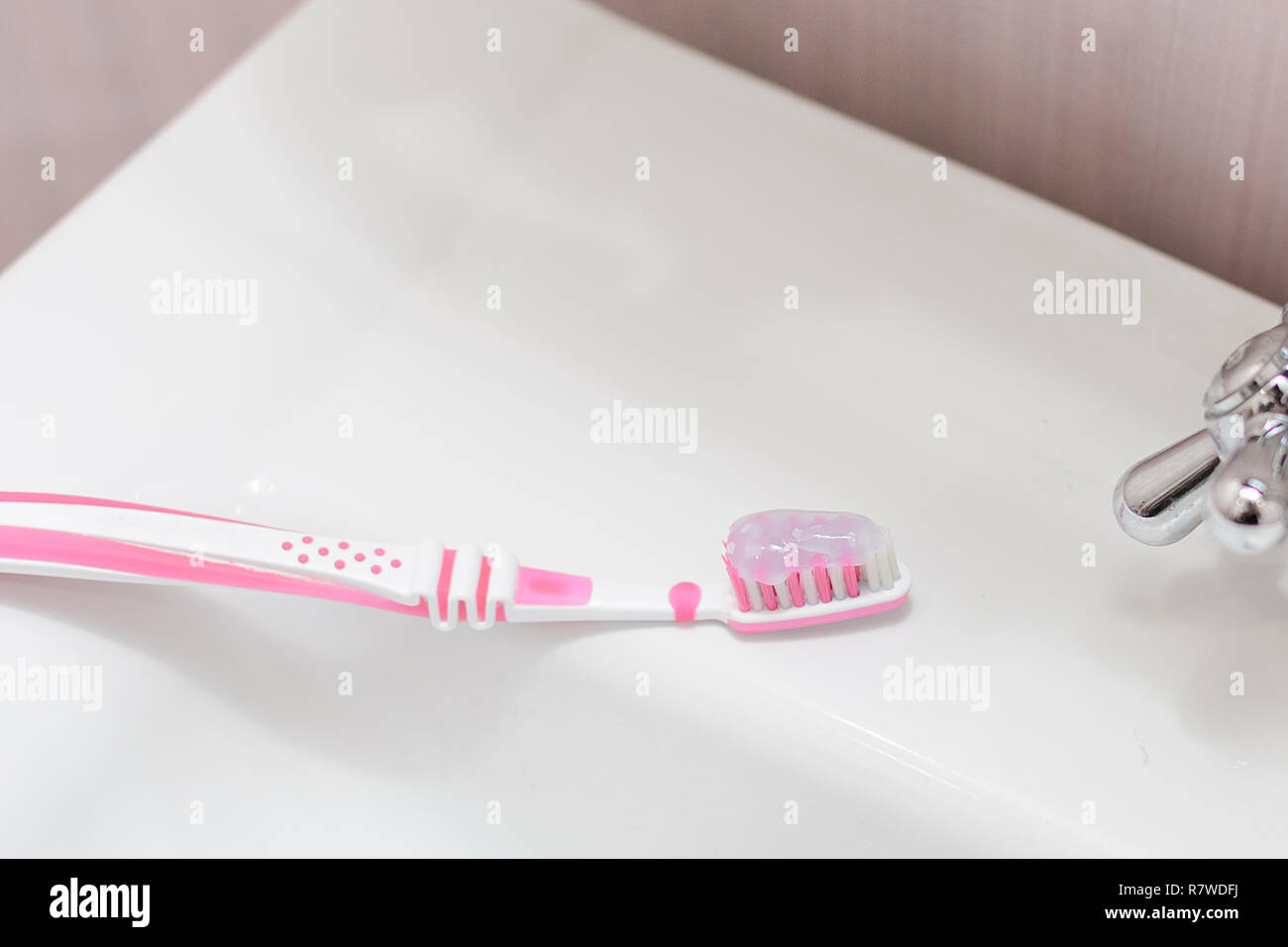 A pink toothbrush with a toothpaste is lying on the washbasin. Small ...