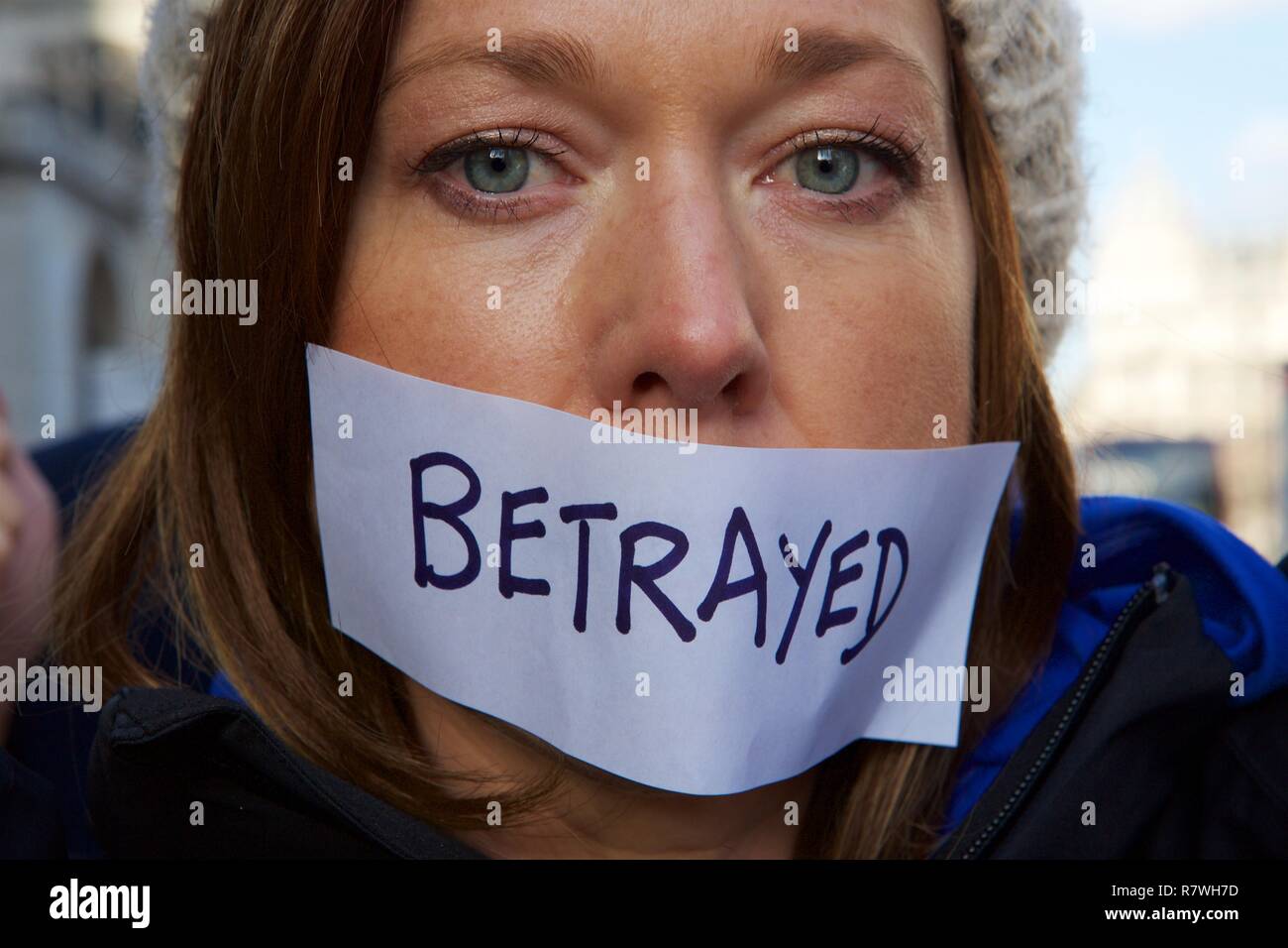 London, UK. Tuesday 11 December 2018 - pro & anti Brexit demonstrators gather to voice their views, after Teressa May delays parliamentary vote on the 'Deal'. A young women walks muted with tape on her lips bearing the word 'Betrayed.' Parliament Buildings in London - UK Credit: Iwala/Alamy Live News Stock Photo