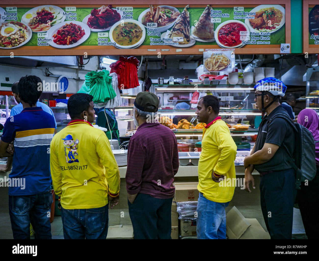 Singapore, Singapore. 11th Dec, 2018. People lined up a food shop in a ''hawker court'' in the Geylang neighborhood. Singapore forced food venders off the street and put them in hawker courts years ago. The Geylang area of Singapore, between the Central Business District and Changi Airport, was originally coconut plantations and Malay villages. During Singapore's boom the coconut plantations and other farms were pushed out and now the area is a working class community of Malay, Indian and Chinese people. In the 2000s, developers started gentrifying Geylang and new housing estate developme Stock Photo