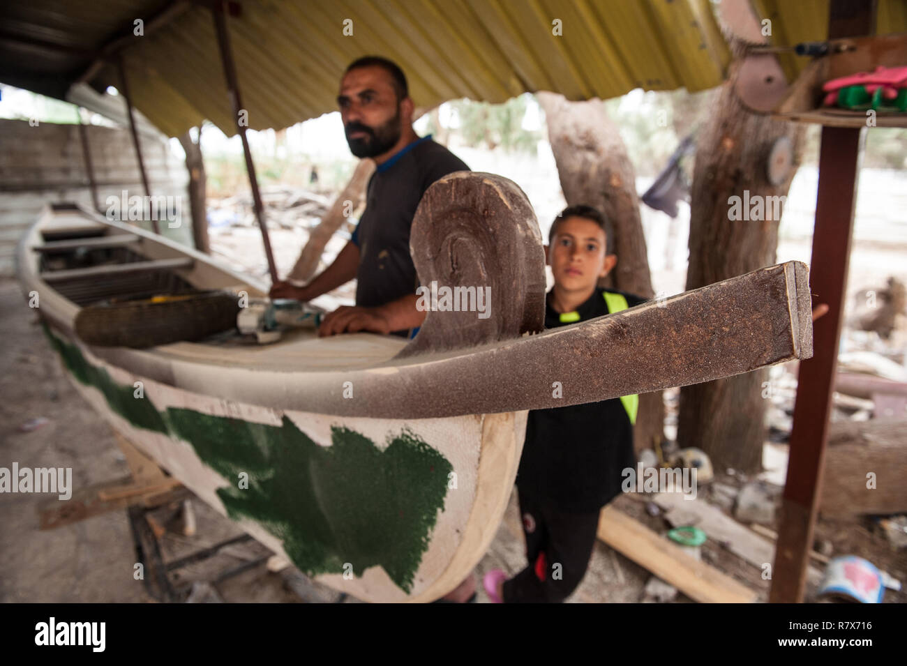 A traditional boat builder with his kid seen in the town of Al-Chibayish on the banks of the Euphrates river in the southern wetlands of Iraq. Climate change, dam building in Turkey and internal water mismanagement are the main causes of a severe drought in the southern wetlands of Iraq. Stock Photo