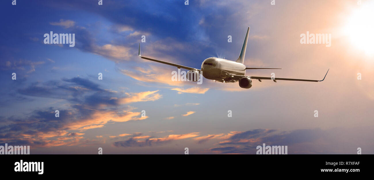 Commercial airplane flying above clouds in dramatic sunset light Stock Photo