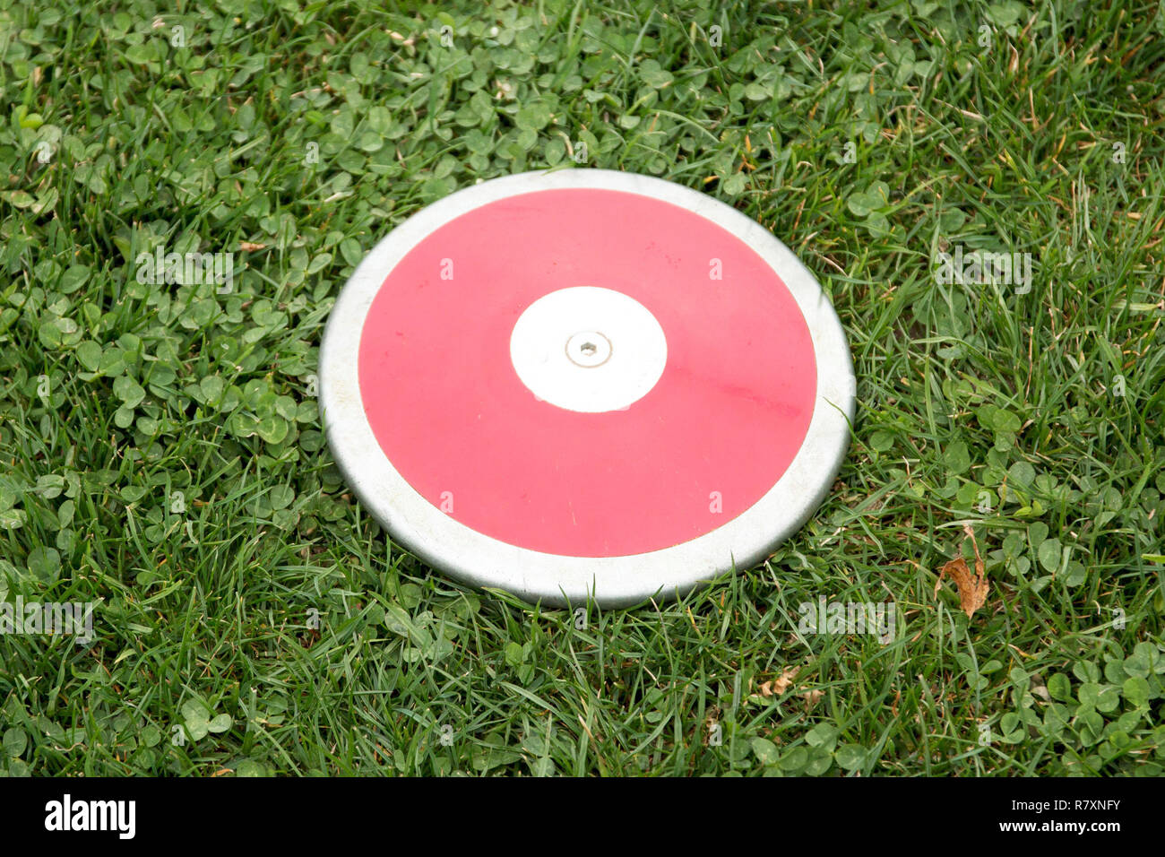 A red girls 1K discus rests on the green grass Stock Photo