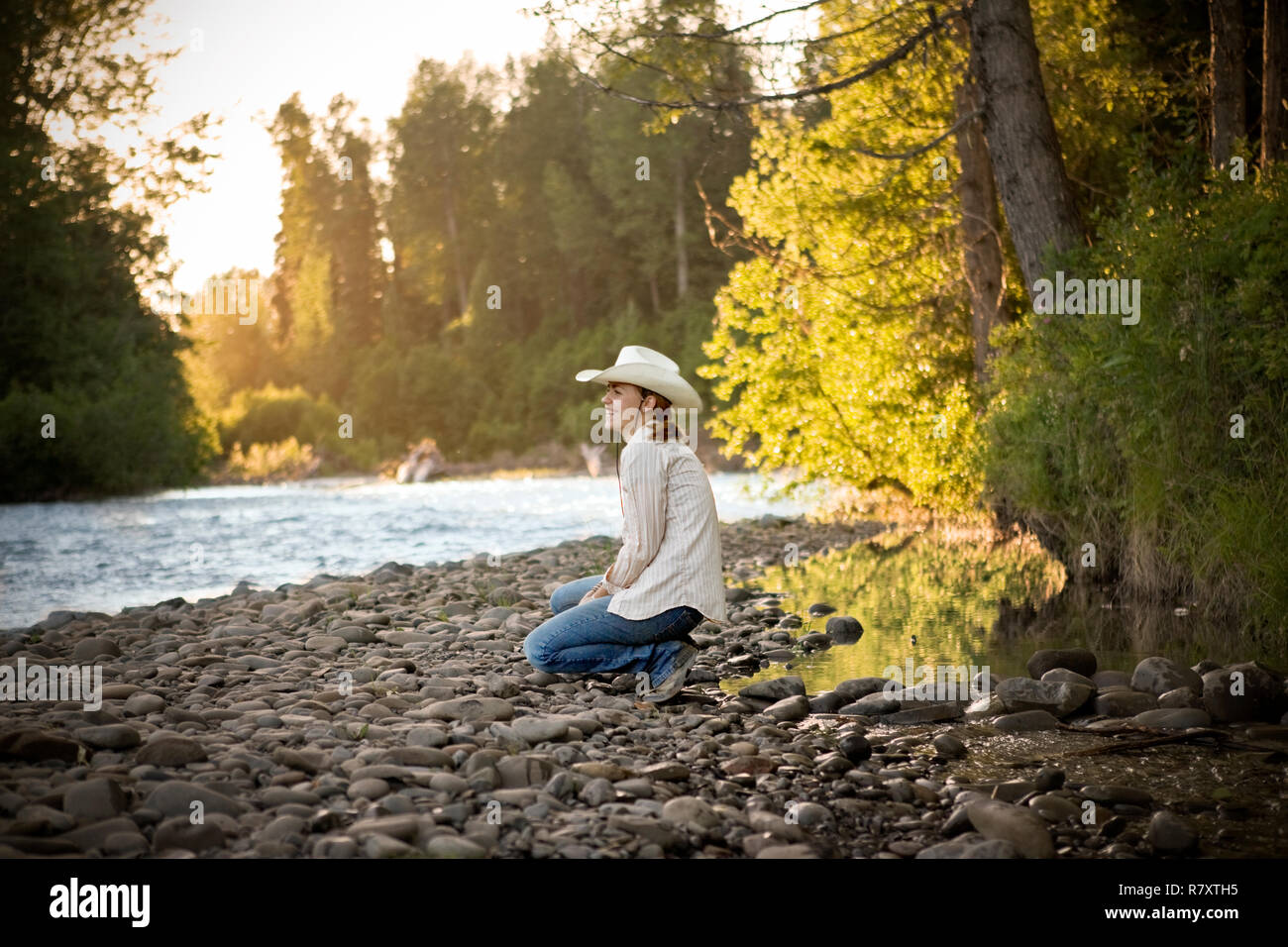 Smiling young woman crouching on a riverbank Stock Photo - Alamy