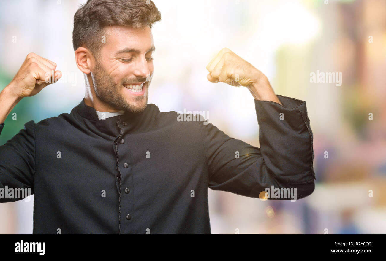Young catholic christian priest man over isolated background showing arms muscles smiling proud. Fitness concept. Stock Photo