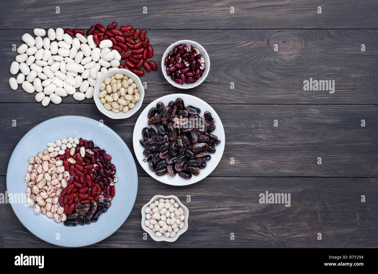 Various dry beans on a wooden background in two bowls and scattered  on the table. Red kidney,pinto, navy  and other  beans. Stock Photo