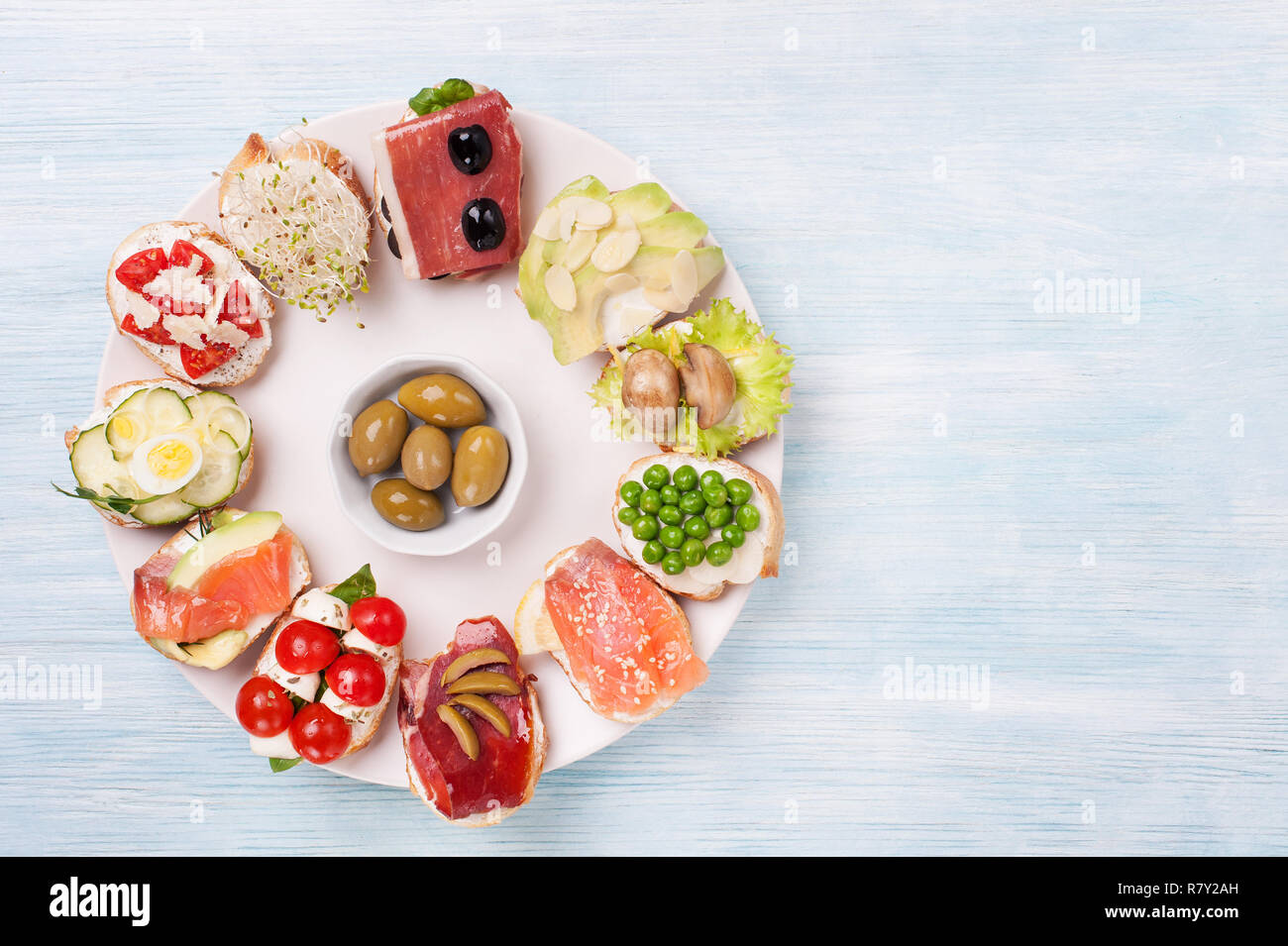 Tasty  canape  with smoked salmon, cucumber,mozzarella, eggs,  mushrooms, olives, avocado, almonds   served on a plate. Stock Photo