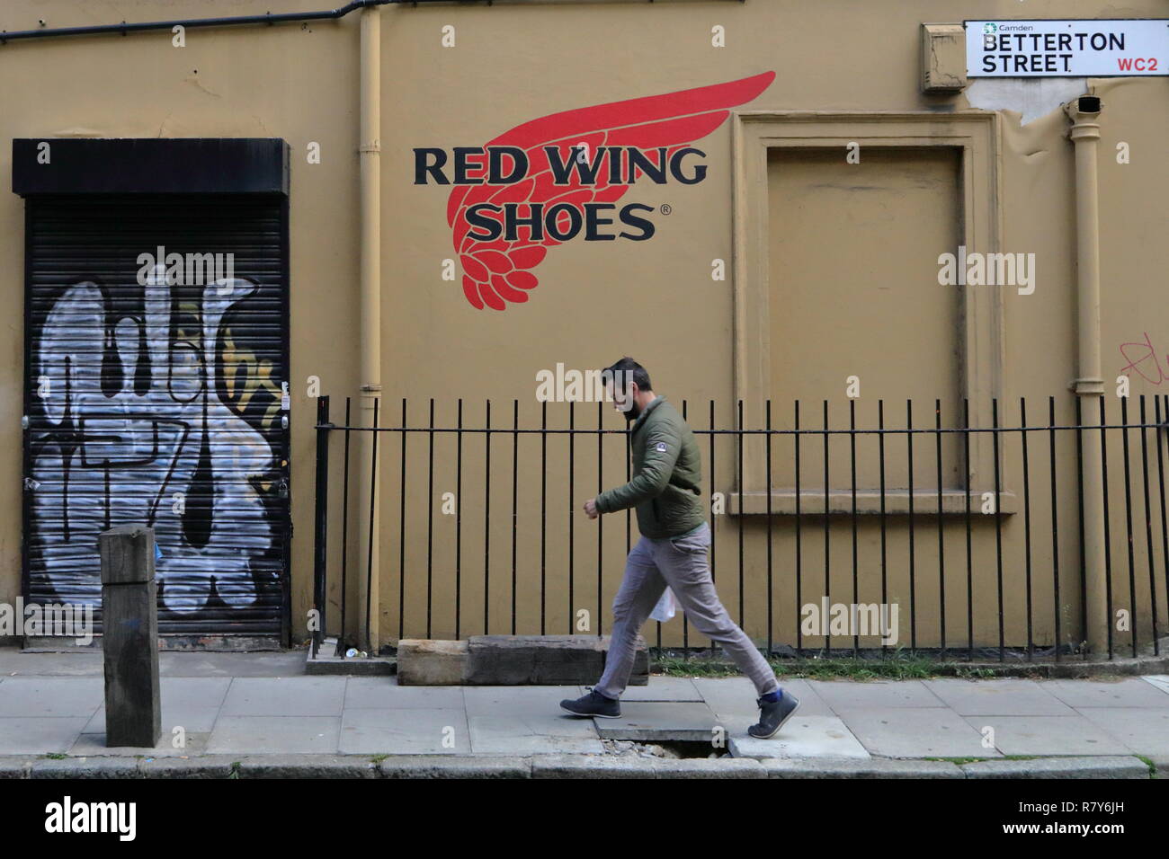 Walking men on the one of the central streets of London. Summer time and small graffiti saying 'red wings shoes' drawn on the wall. Stock Photo