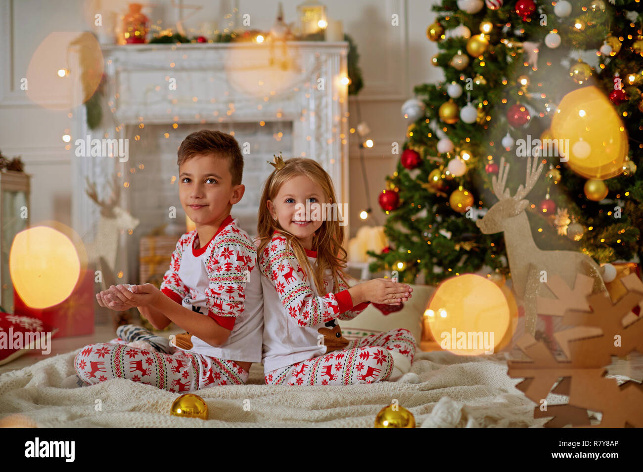 Small children laugh near the Christmas tree behind the green doors and hold in their hands not dawning snow Stock Photo