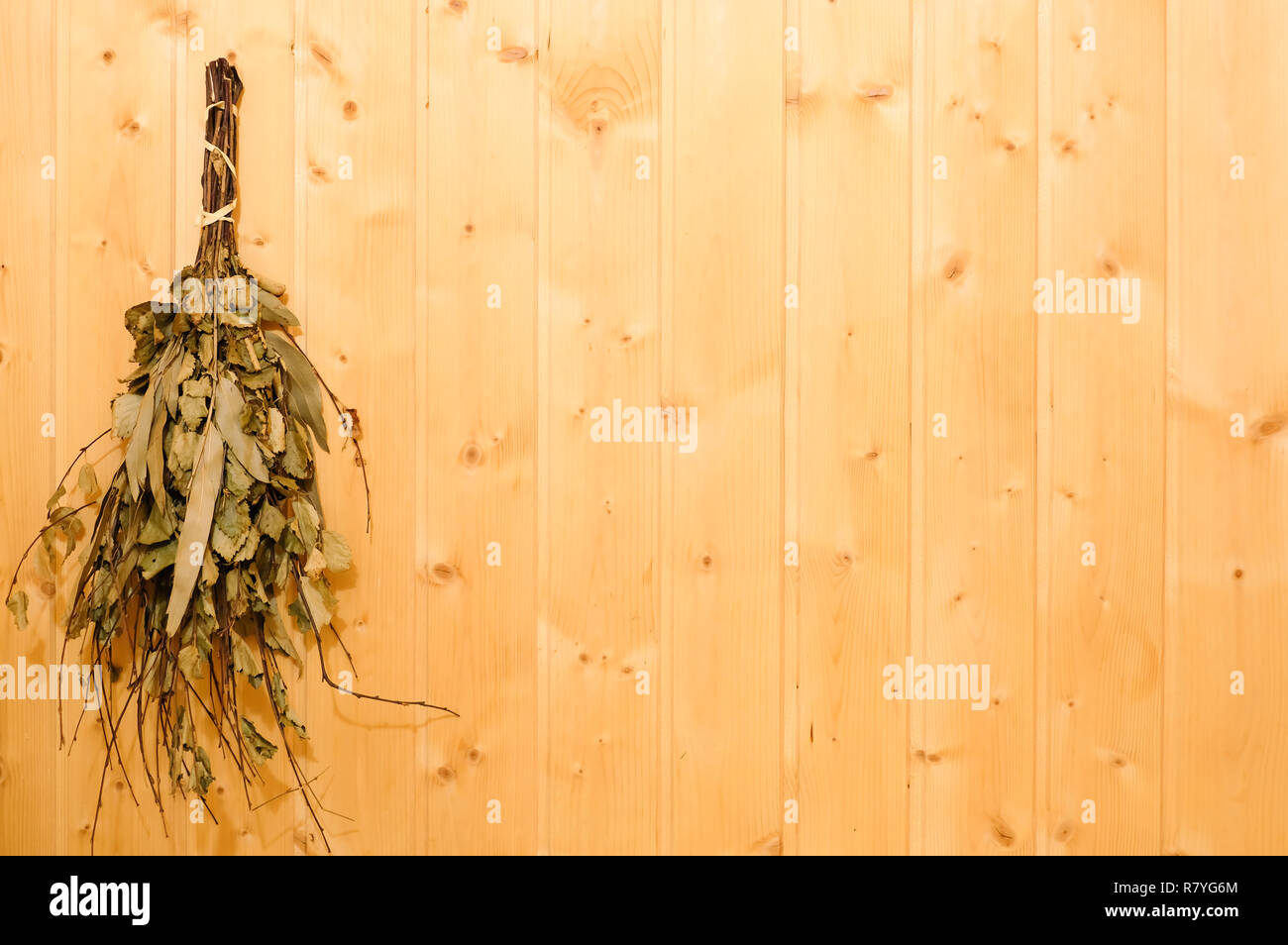 The birch broom hangs in a sauna or bath on a wooden wall. Rest and relaxation in the spa to keep warm in the cold winter Stock Photo