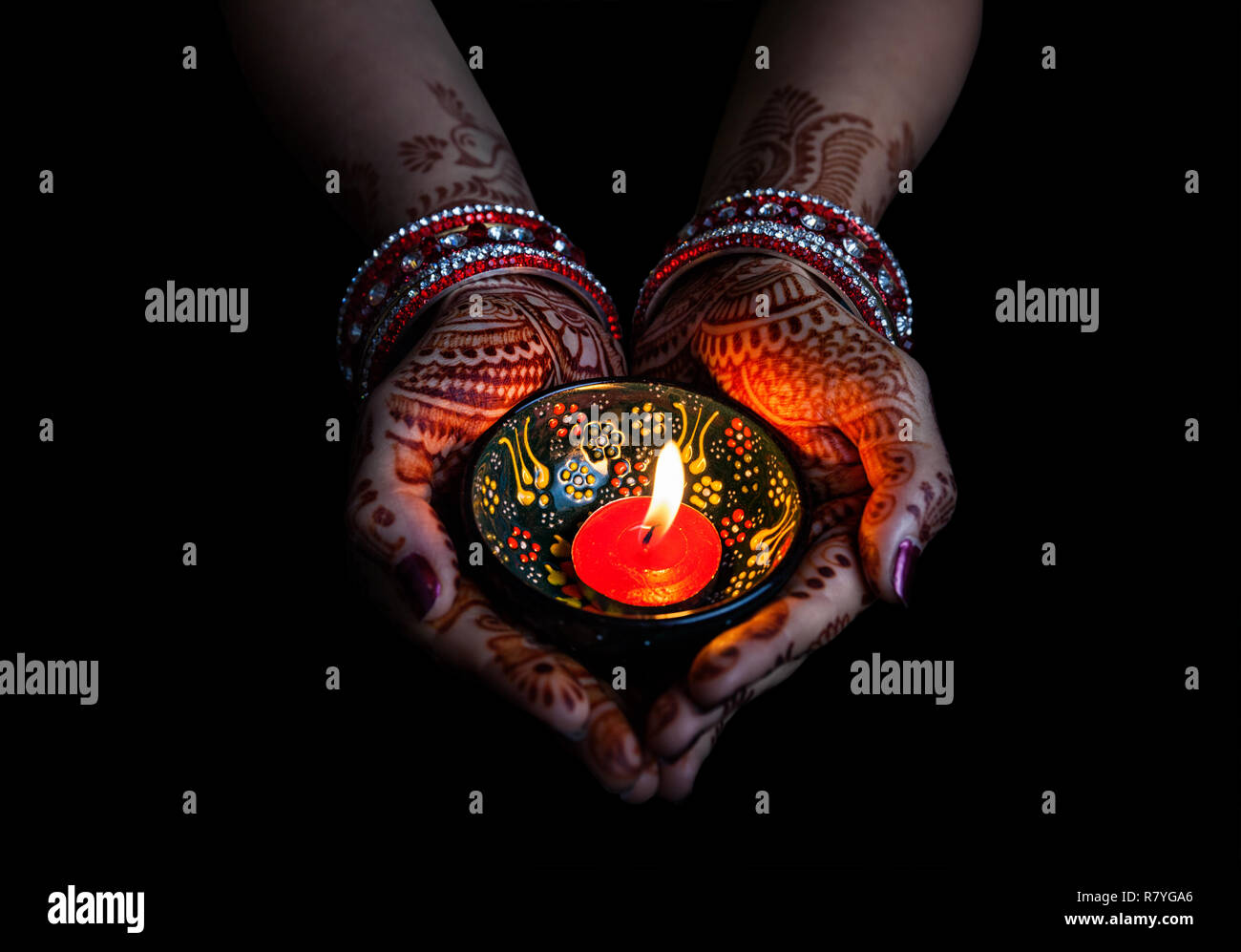 Woman hands with henna holding lit candle isolated on black background with clipping path Stock Photo