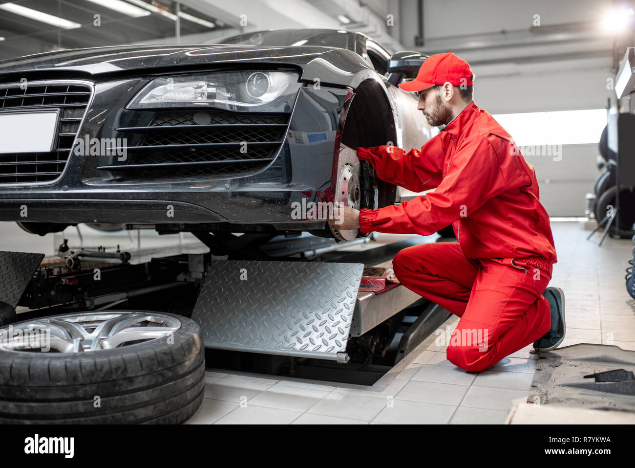 Auto mechanic in red uniform servicing sports car checking front brakes
