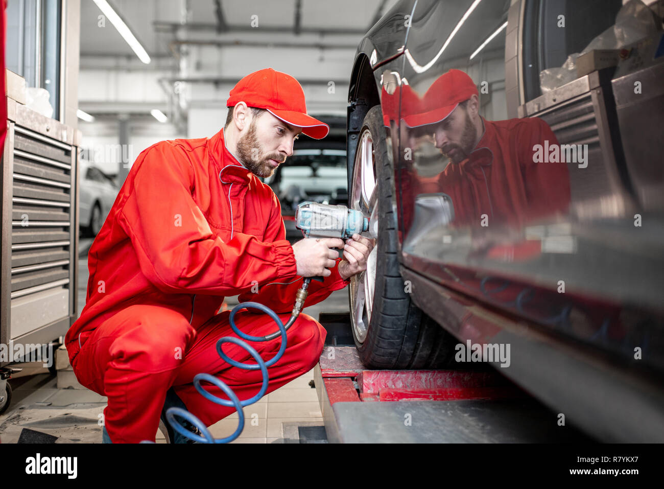 ar service worker in red uniform changing wheel of a sport car at the tire mounting service Stock Photo