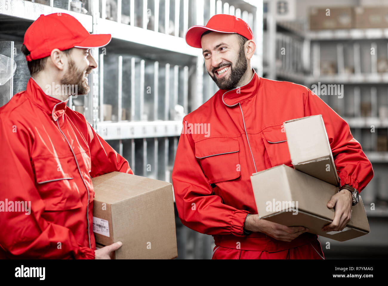Two handsome warehouse workers in red uniform standing with boxes in