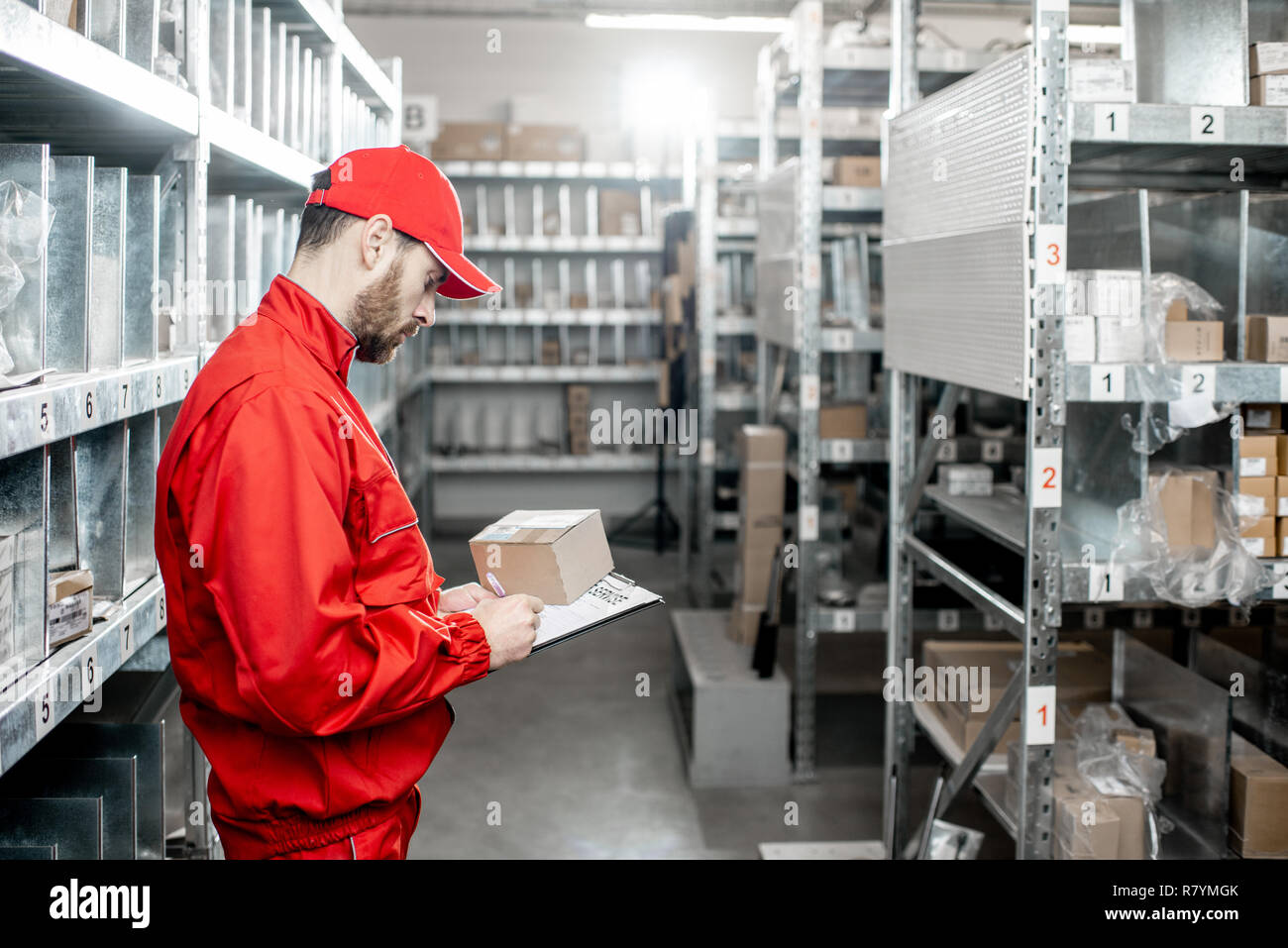 Warehouse worker in red uniform filling some documents checking goods