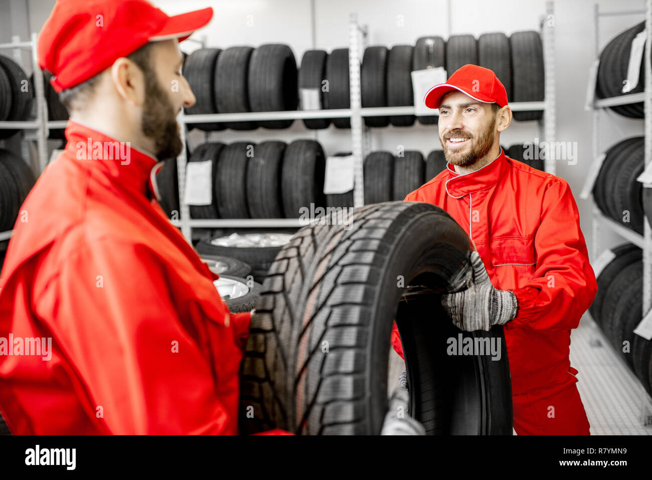 Two men in red uniform working in the warehouse with new car tires Stock Photo