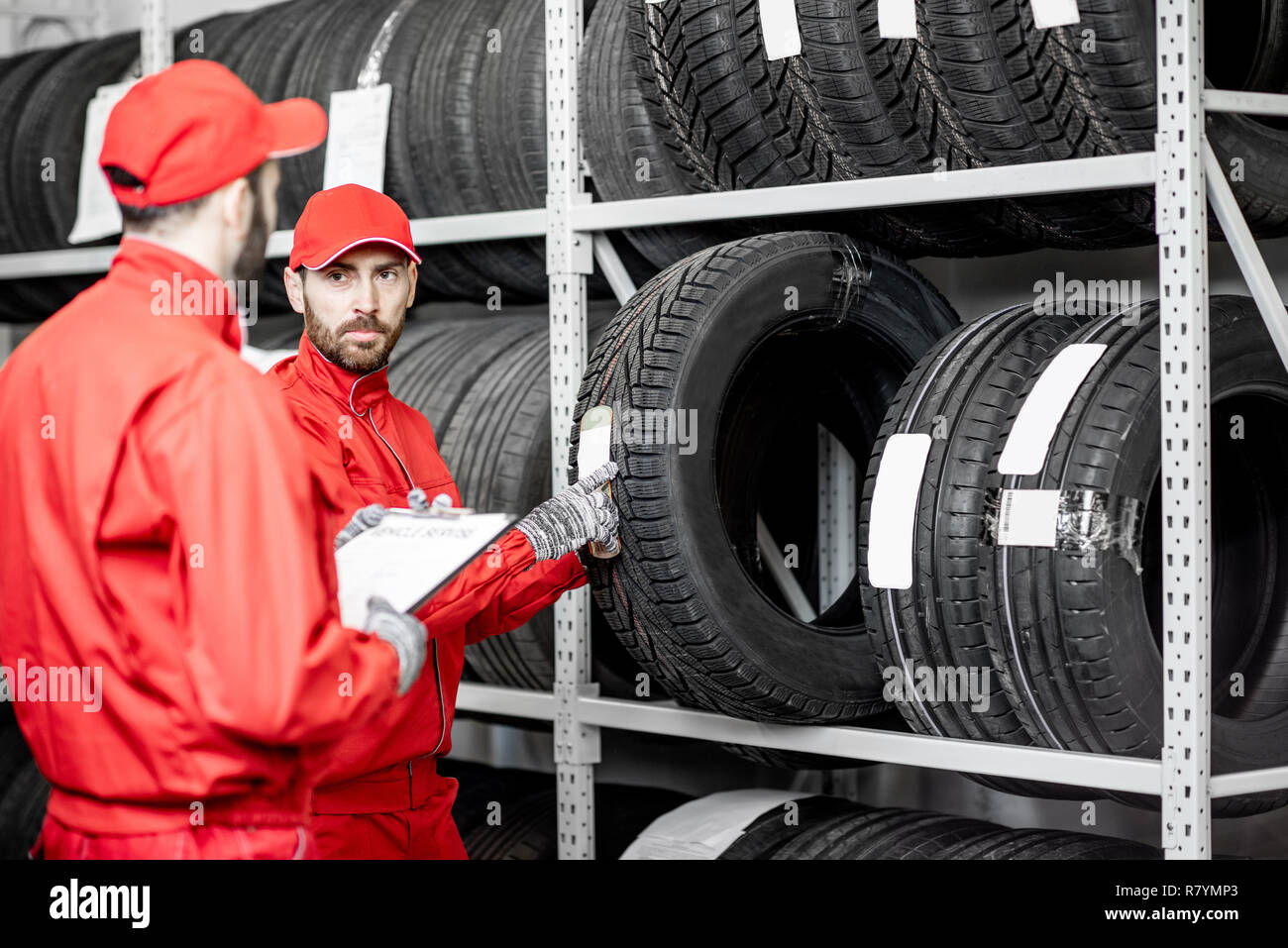 Two men in red uniform working in the warehouse with new car tires Stock Photo