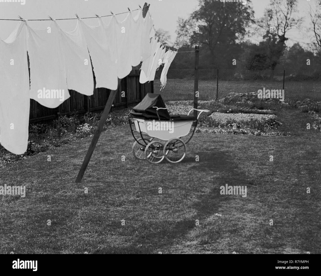 1960s, historical, washing hanging out on a clothes line to dry naturally in the fresh air and a traditional coach-built pram standing outside in a back garden, England, UK. Stock Photo