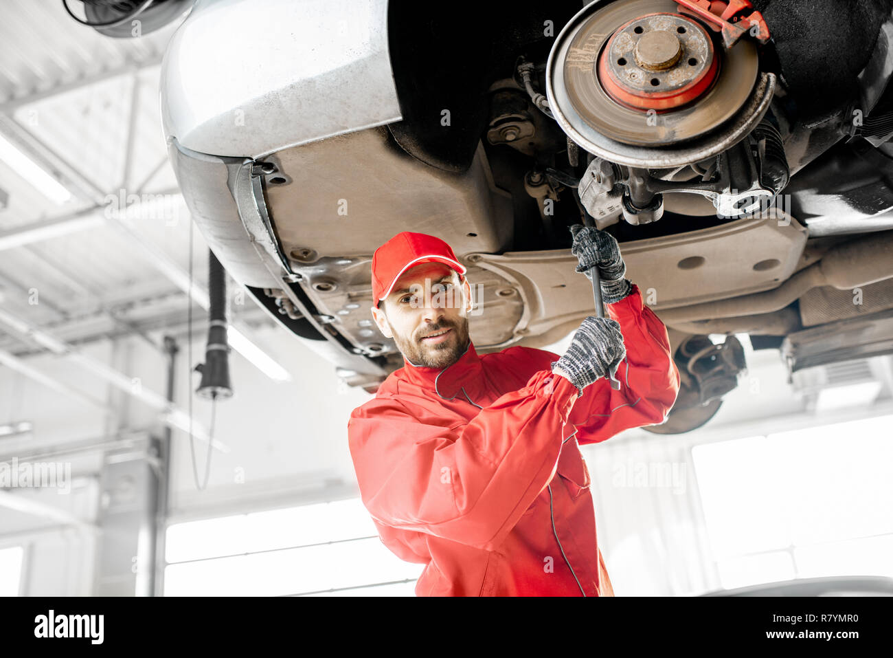Auto mechanic in red uniform diagnosing car on the hoist at the car
