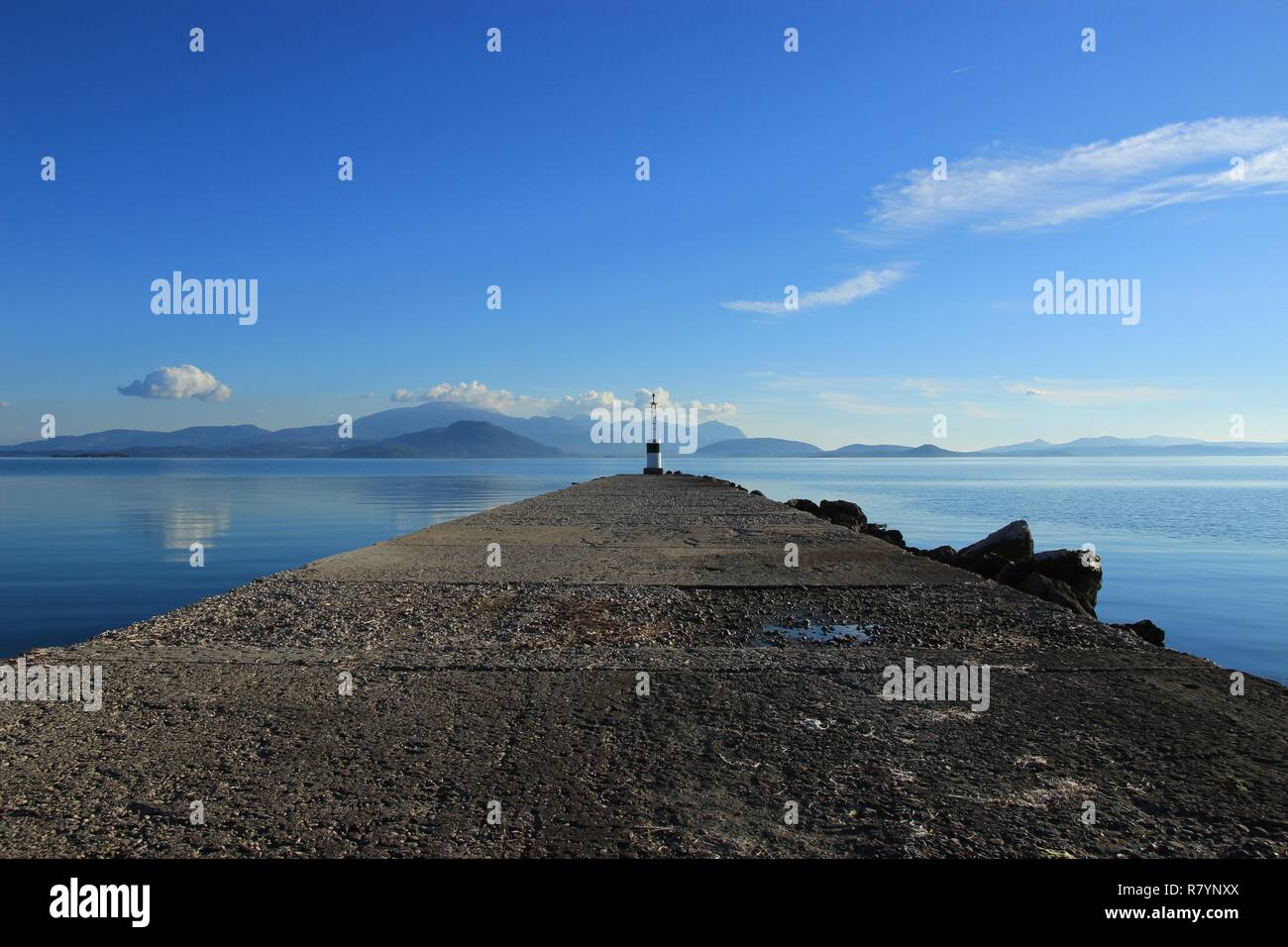 Beacon at the end of pier at Koronisia village in Ambracian gulf, Epirus Greece, calm blue sea, clouds in the sky Stock Photo