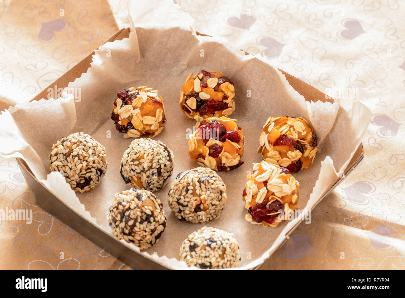 Two kinds of handmade energy balls are lying in cardboard box on wrapping paper. Stock Photo