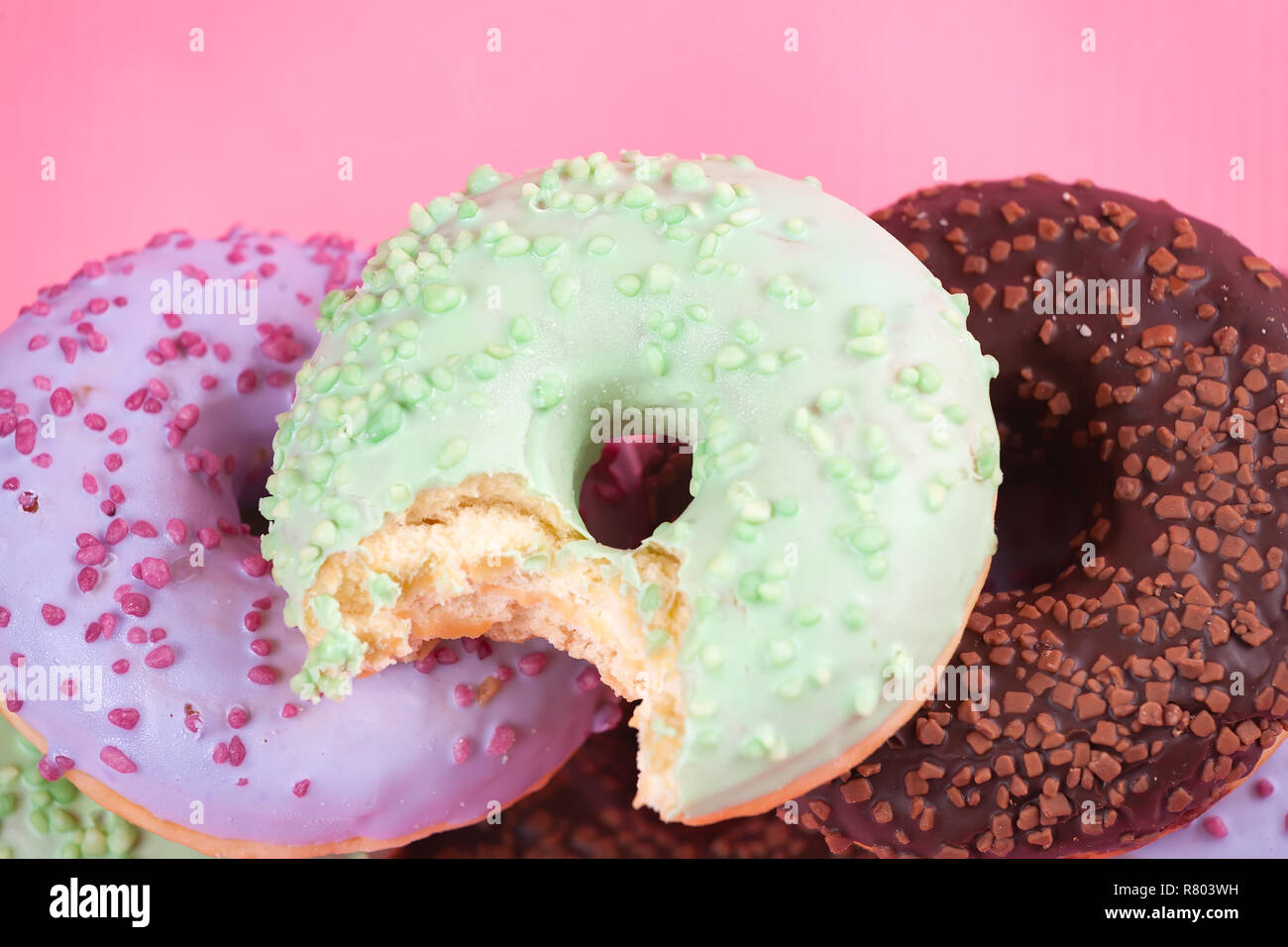 Sweet colorful tasty donuts with icing and sprinkles on pastel pink ...