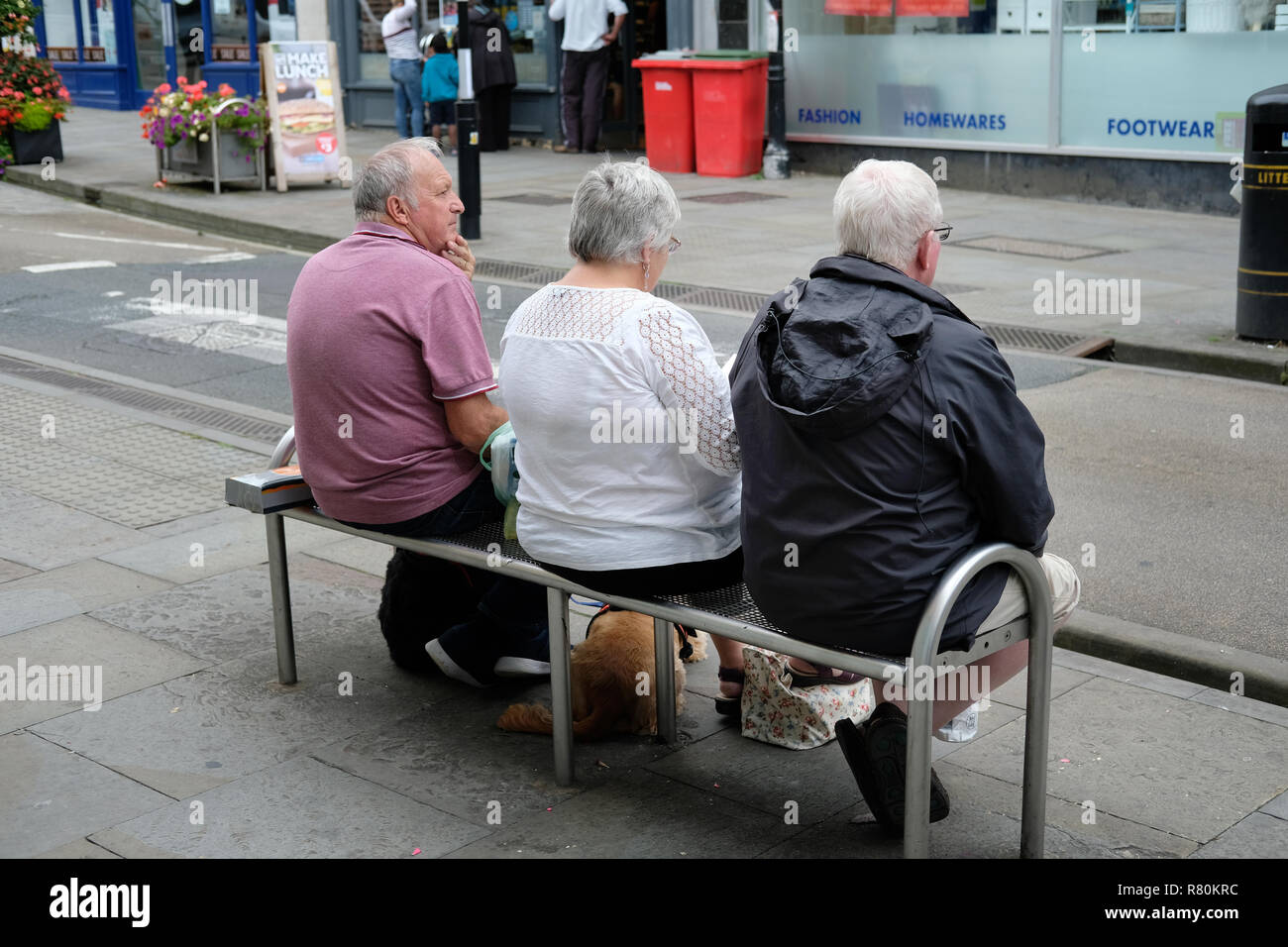 Three pensioners sitting on a bench on a hight street in Wells, Somerset. Stock Photo