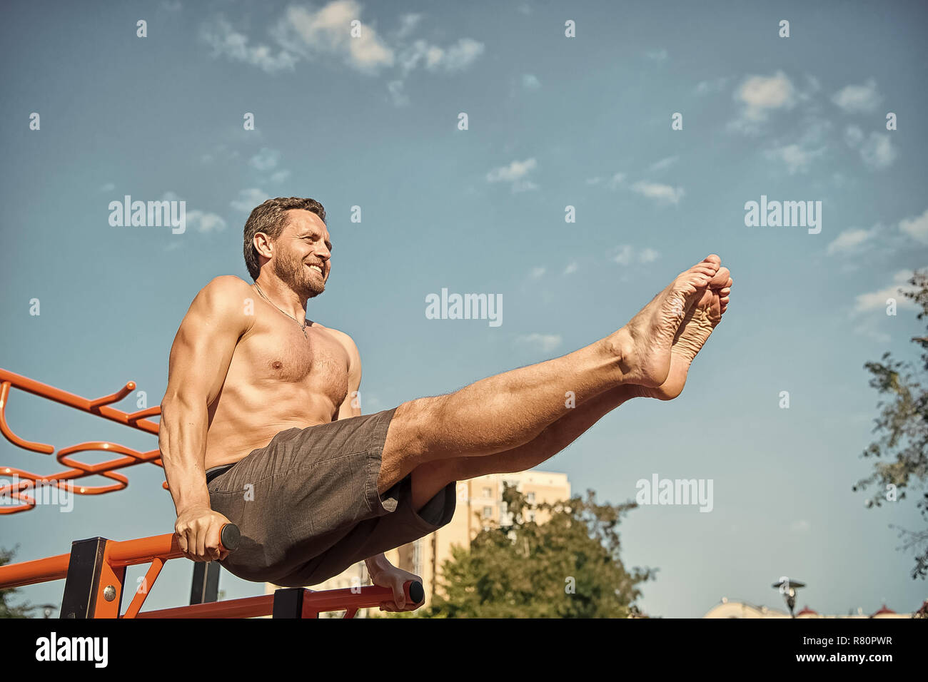 Sportsman exercising on parallel bars outdoors on blue sky. Man ...