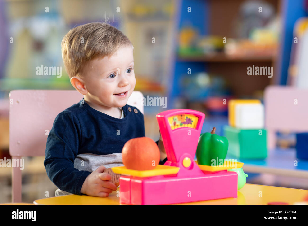 Little child boy sits at table and plays with toy scales in playroom Stock Photo