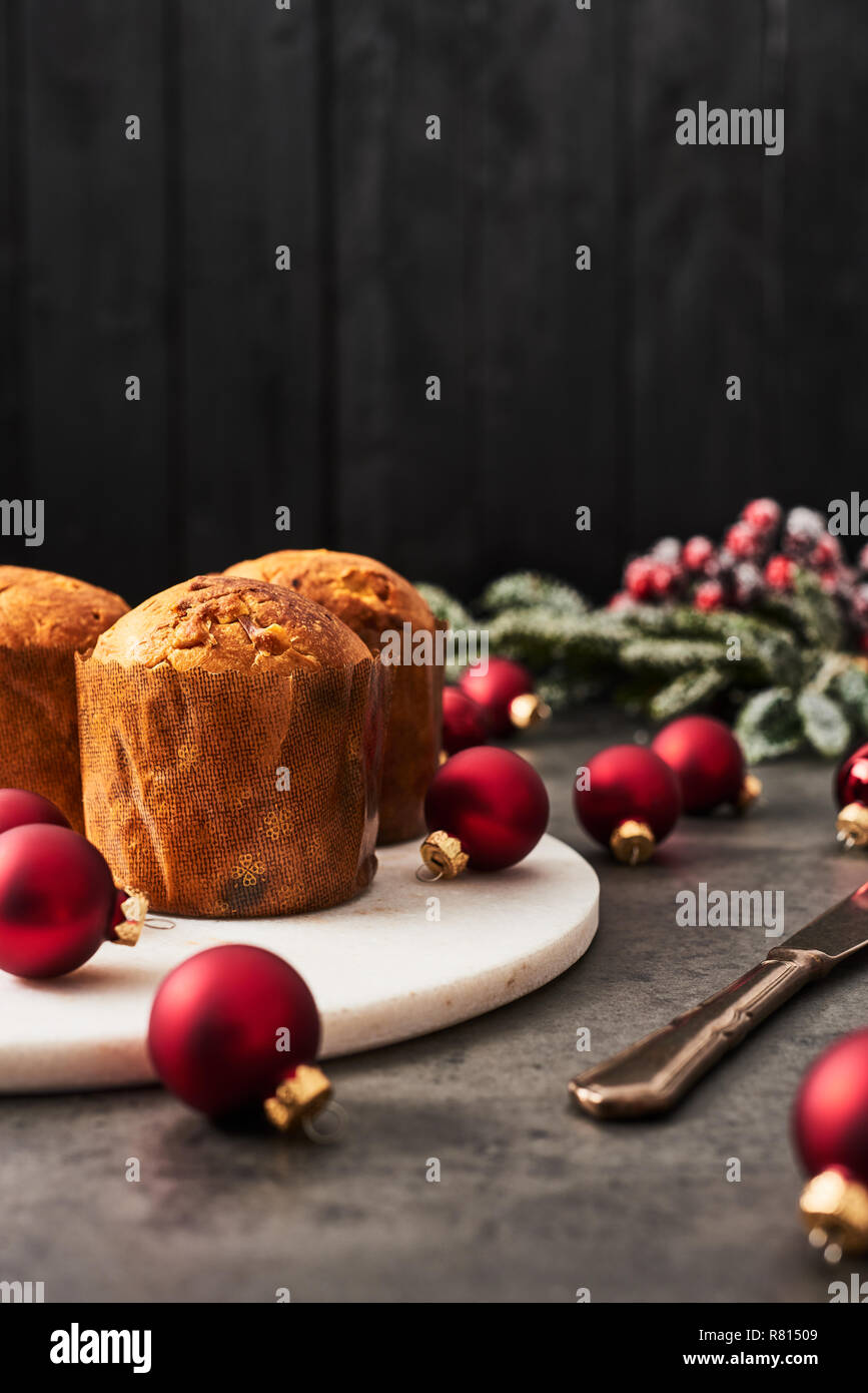 Traditional Christmas mini Panettone with raisins and dried fruits on white marble serving plate surrounded by red Christmas baubles on concrete table Stock Photo