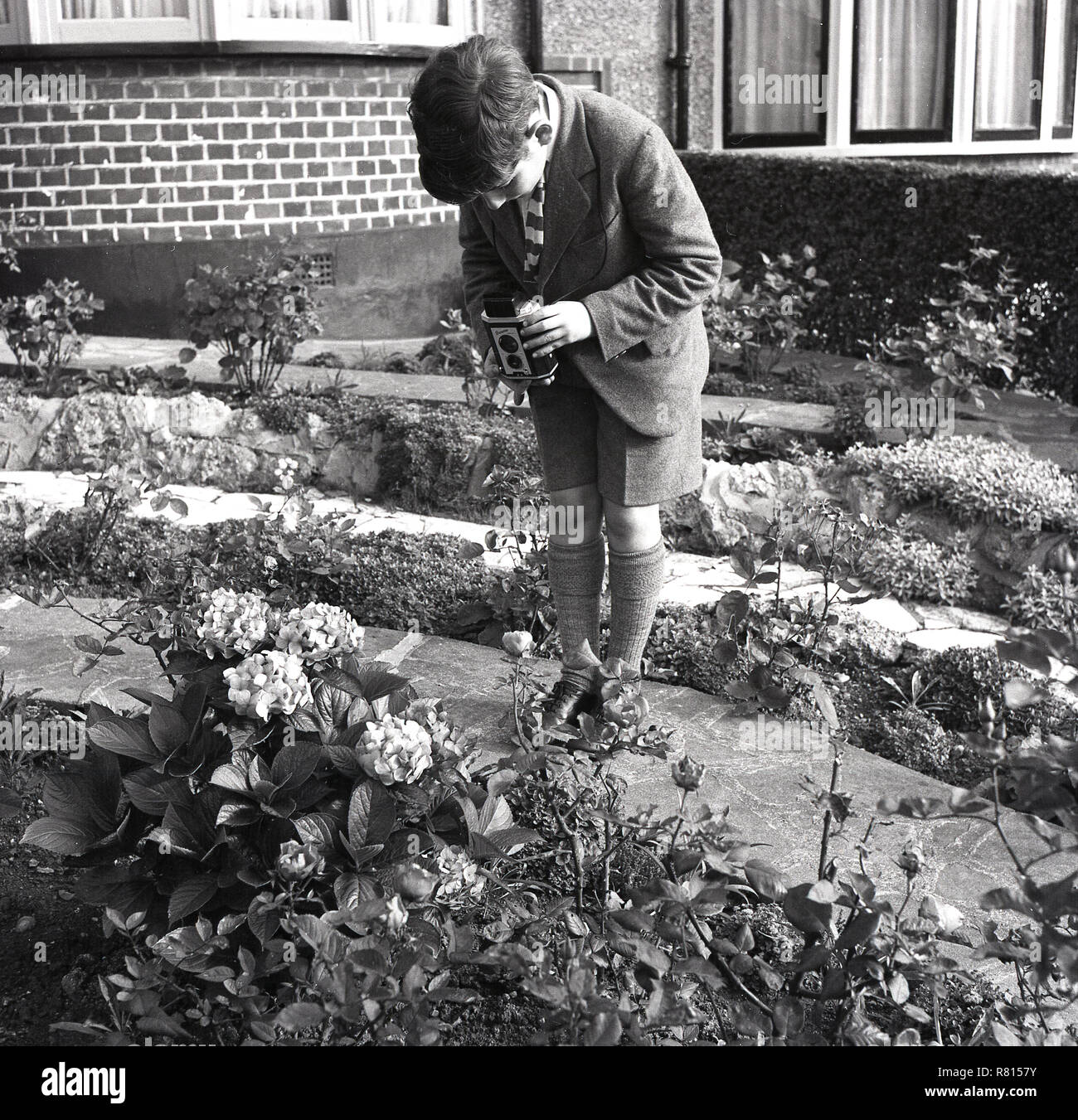 1950s, historical, film photography, a schoolboy outside a floral garden taking pictures of flowers with a Kodak 'Brownie' reflex film camera, England, UK. A fixed focus, twin-lens camera, it was a simple but popular camera of the era, particularly with those starting out in photography. Stock Photo