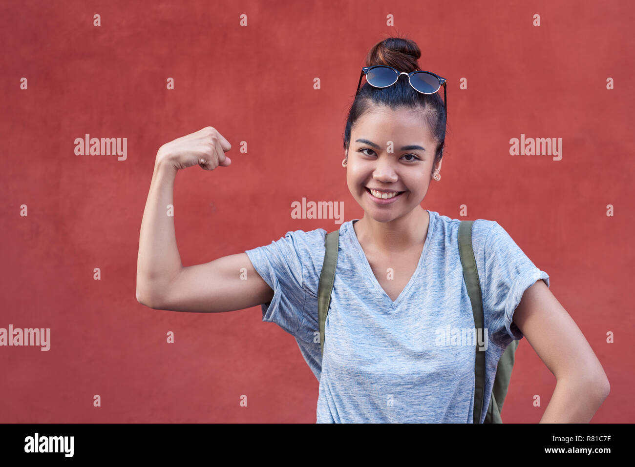 Young Asian woman smiling while humorously flexing her bicep outside Stock Photo