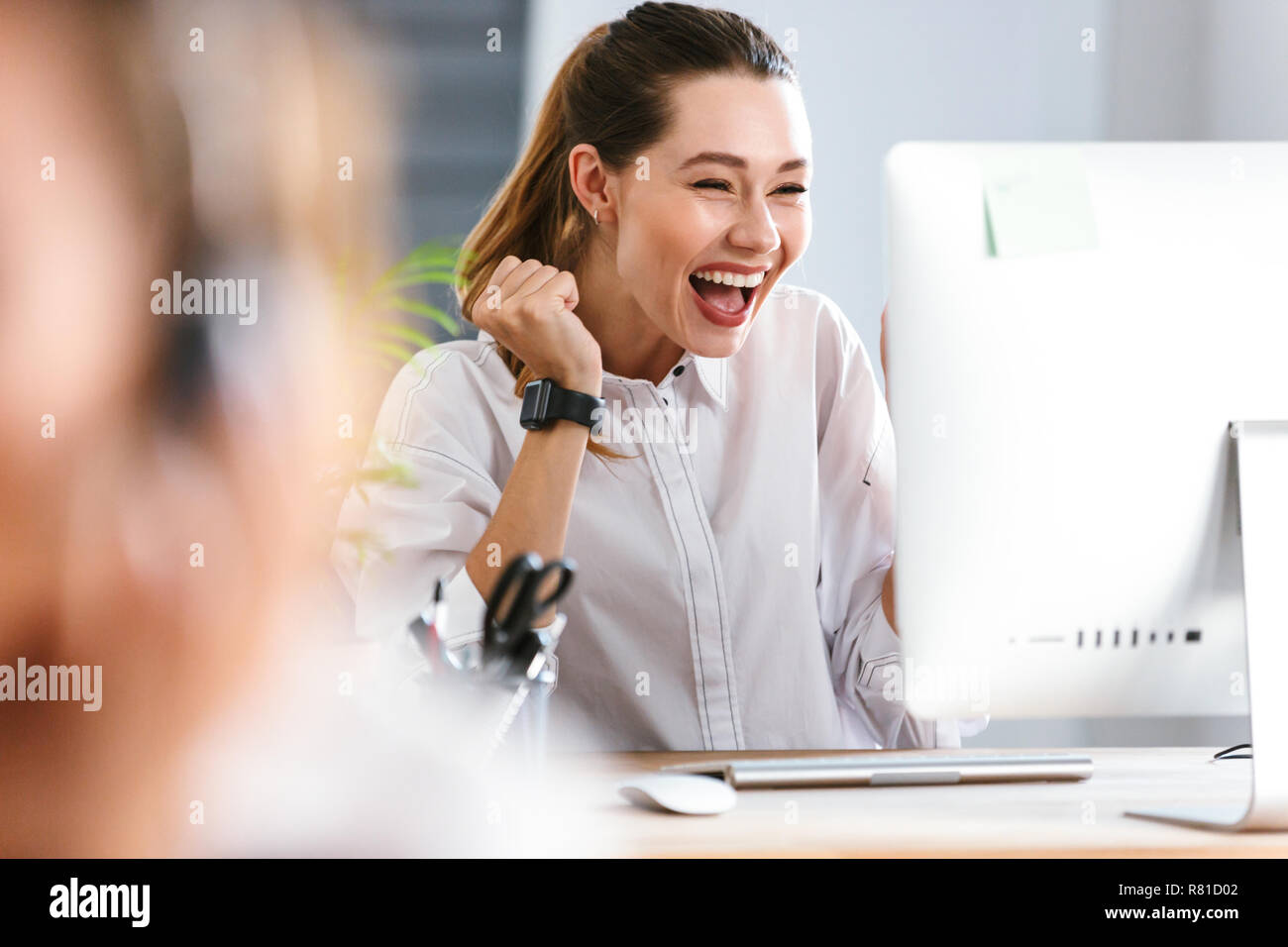 Happy young woman dressed in shirt sitting at her workplace at the ...