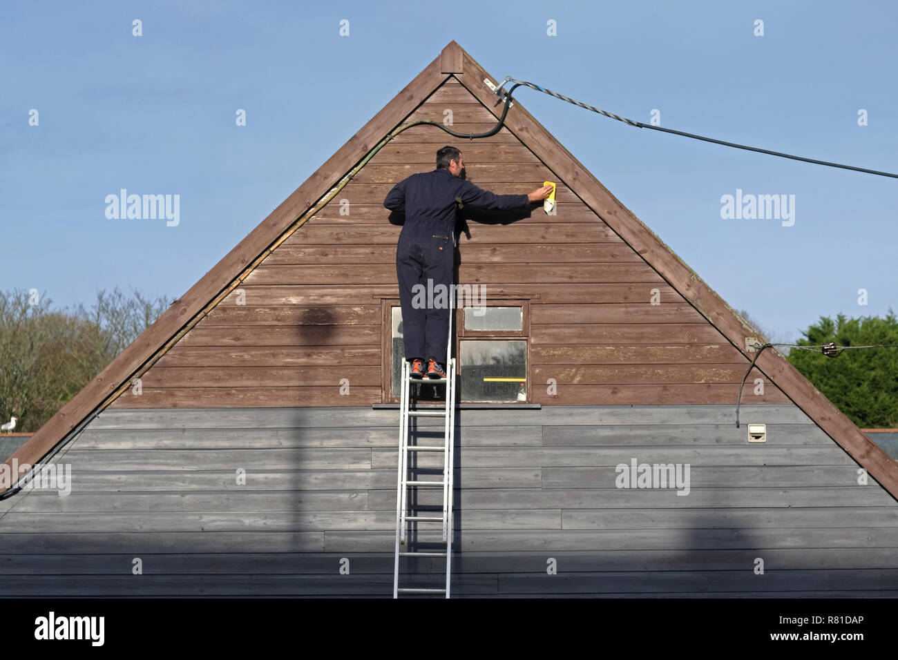 A carpenter, decorator, sanding down the exterior woodwork of a building. Stock Photo