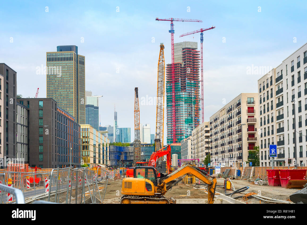 Excavator, cranes and construction equipment at construction site in downtown at street with buildings and skyscaraprers of modern architecture, Frank Stock Photo